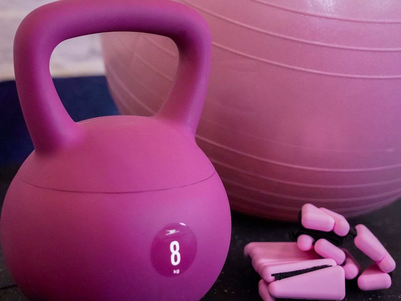 A pink 8kg kettlebell beside a stability ball and a set of pink hand weights