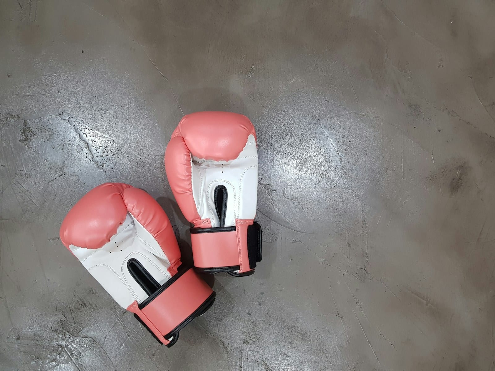 A pair of coral pink and white boxing gloves lying on a grey concrete floor, seen from above