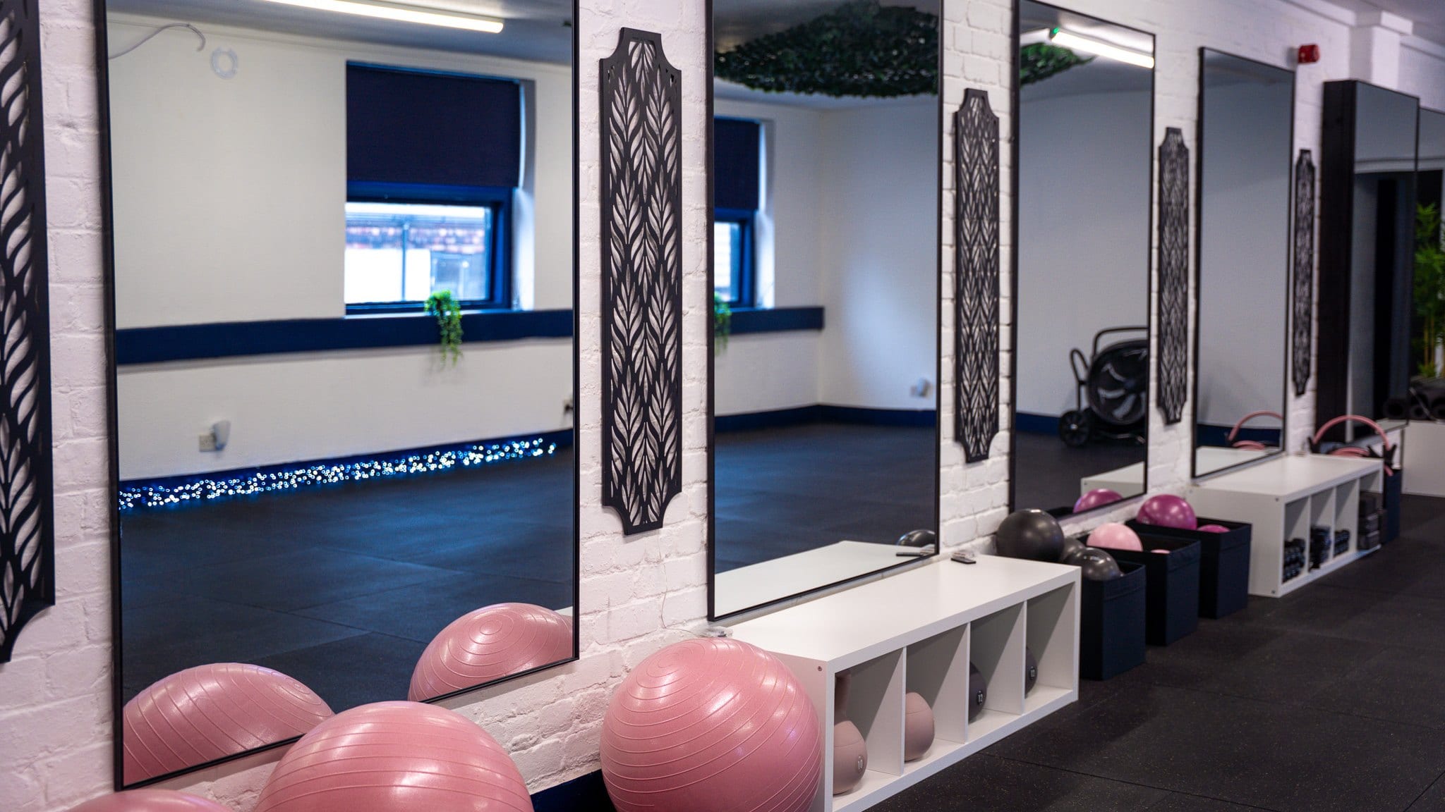 The studio's mirrored wall, with pink stability balls, weighted balls and white storage benches running along it
